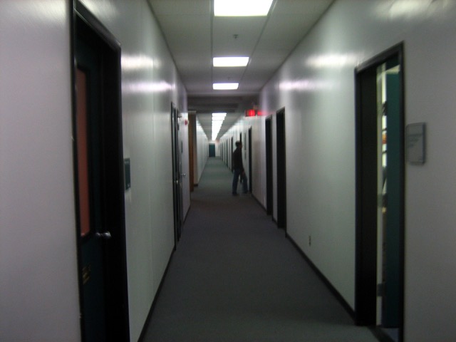 Photo of a blurry figure entering an office in the middle of an otherwise empty hallway.